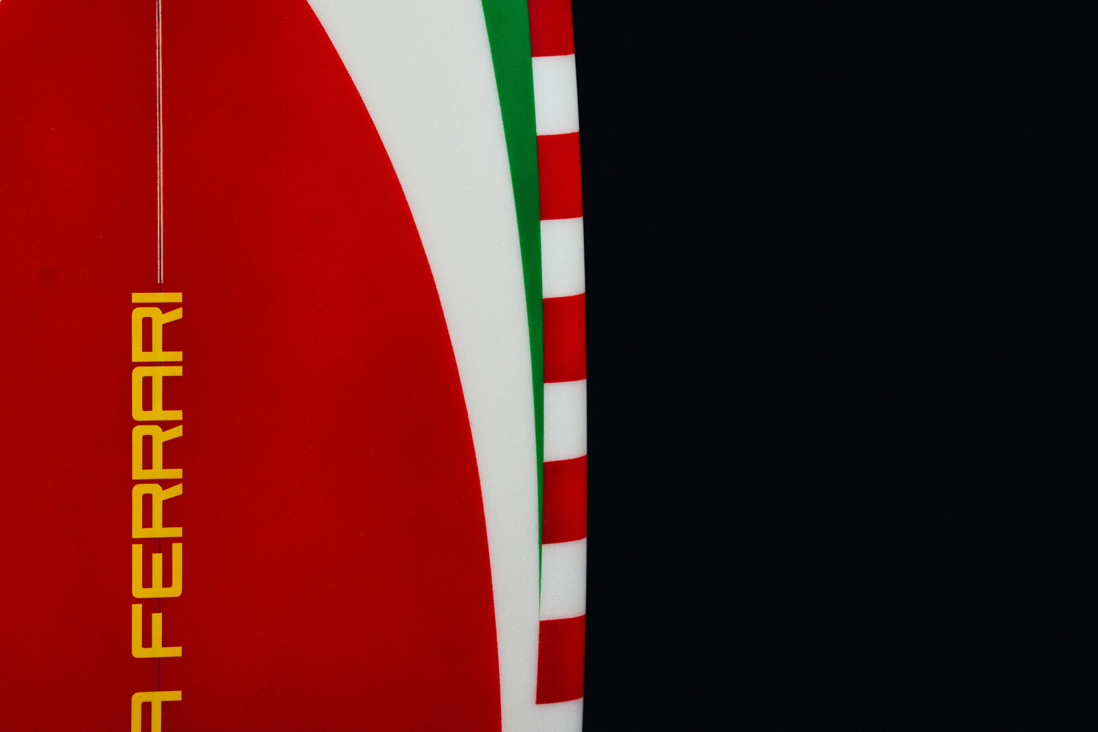 Side view of the Ferrari Limited Edition surfboard with red and white striped borders. / Vista laterale della tavola da surf Ferrari in edizione limitata con bordi a strisce rosse e bianche.